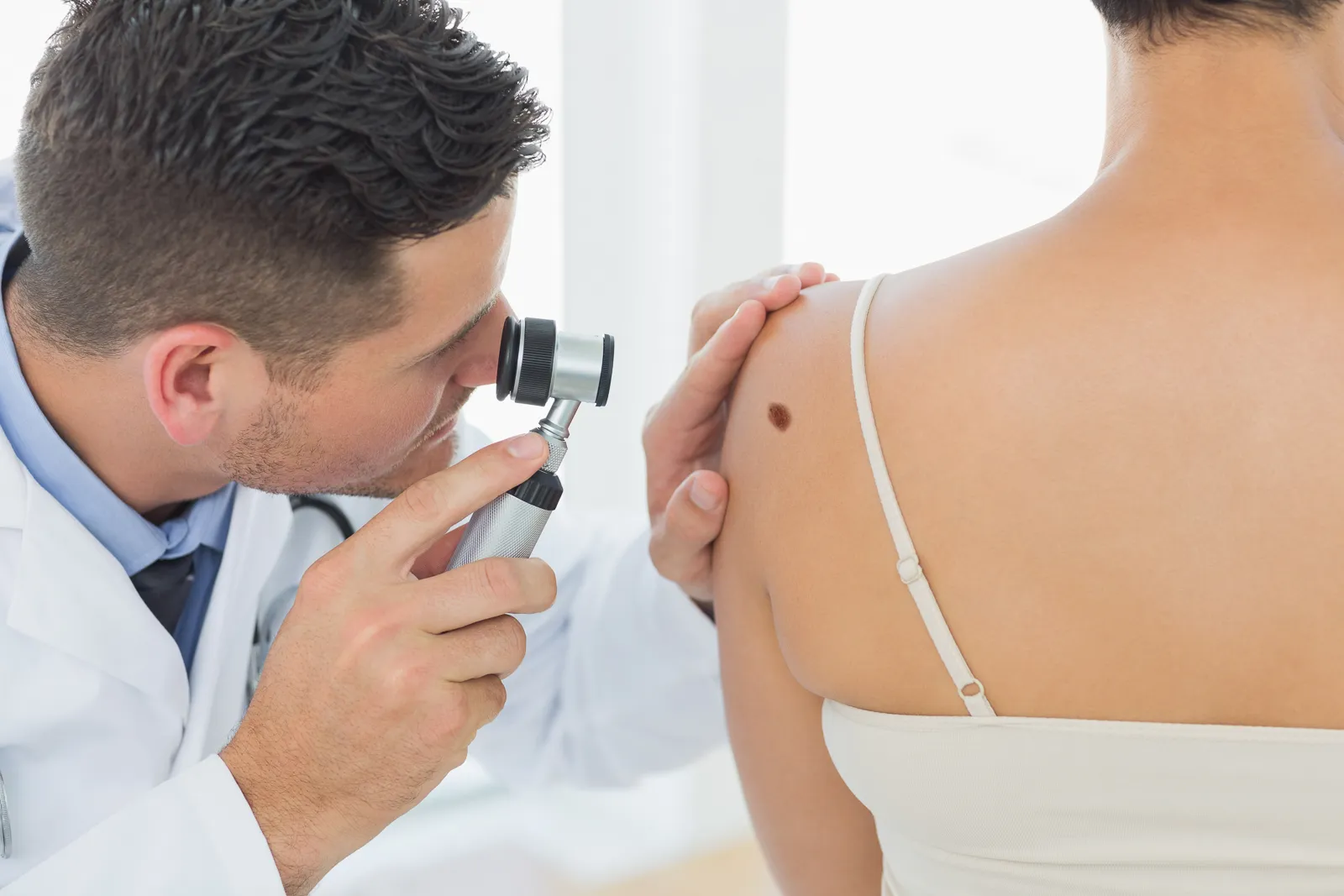 Dermatólogo examinando con un dermatoscopio un lunar en el hombro de una paciente